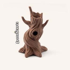Peut inclure: Une sculpture de souche d'arbre creuse de couleur brune avec une surface texturée et noueuse, présentant une ouverture centrale et deux branches latérales. Le texte SPOODSCAPES est imprimé verticalement en noir sur le côté gauche de l'objet.