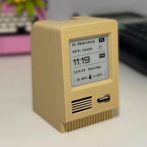 May include: A beige e-paper desktop companion with a screen displaying the time, weather, and date. The device has a retro computer design with the text "E-PAPER DESKTOP COMPANION" above it and "PAPER WIDGET" below. The device is from Rat Lab Studio.