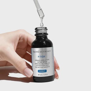 May include: A black skincare serum bottle with a dropper dispensing a clear liquid. The bottle has a white label with the text "SKINCEUTICALS P-TIOX" and other product information. The bottle contains 1 fl oz of serum.