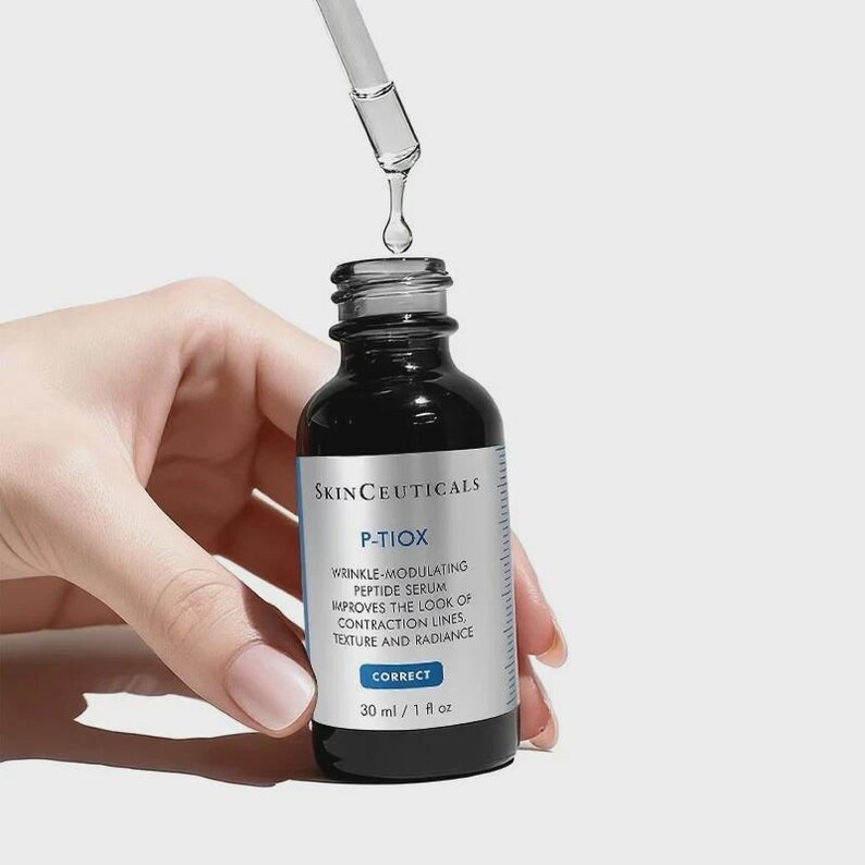 May include: A black skincare serum bottle with a dropper dispensing a clear liquid. The bottle has a white label with the text "SKINCEUTICALS P-TIOX" and other product information. The bottle contains 1 fl oz of serum.