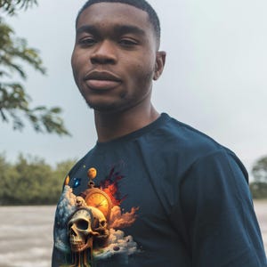 May include: Navy blue t-shirt featuring a surreal graphic of a skull, pocket watch, and clouds. The design incorporates vibrant colors like orange, yellow, and blue. The shirt is a classic crew neck style.