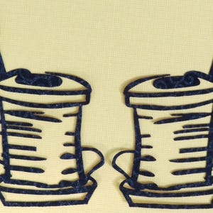 May include: Two dark blue, stylized coffee cup cutouts with a spoon and a wavy line on a light yellow background. The cups have a handle and a lid. The design is simple and graphic.