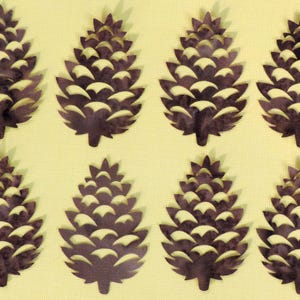 May include: Eight dark brown pine cone cutouts with white accents are arranged on a light yellow background. The pine cones have a detailed, layered design, suggesting a craft or decorative theme.