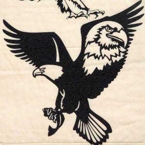 May include: Black and white silhouette of an eagle with its wings spread. The eagle is in flight and has a fierce expression on its face.