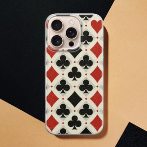 May include: A clear phone case with a playing card design. The pattern includes red diamonds and hearts, black clubs and spades, and a cream-colored background. The phone case has a camera bump.