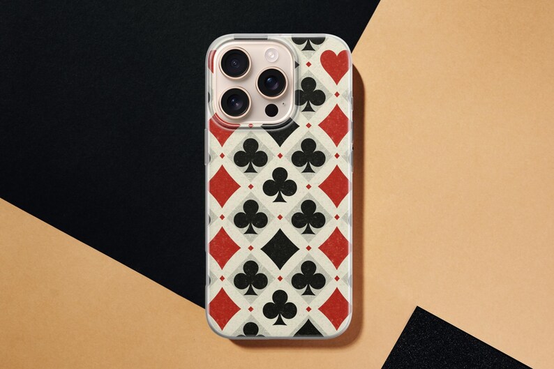 May include: A clear phone case with a playing card design. The pattern includes red diamonds and hearts, black clubs and spades, and a cream-colored background. The phone case has a camera bump.