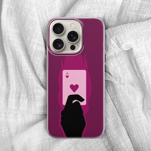 May include: A magenta phone case featuring a silhouette of a hand holding the Ace of Hearts playing card. The card is light pink with a red heart symbol. The case has a dark magenta background with a flame design.