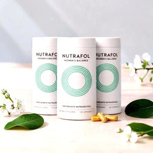 Puede incluir: Tres envases cil&iacute;ndricos blancos de "Nutrafol Women's Balance", nutrac&eacute;uticos para el crecimiento del cabello. Cada envase tiene un dise&ntilde;o circular turquesa y el texto "Hair Growth Nutraceutical" y "120 Capsules". Varias c&aacute;psulas doradas est&aacute;n delante de los envases.