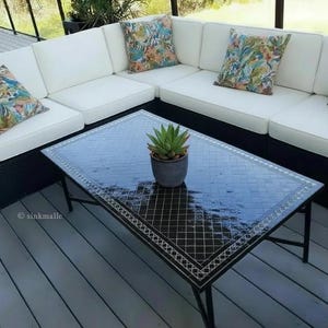 May include: An outdoor corner sofa with white cushions and patterned throw cushions. A black coffee table with a mosaic tile top and a potted succulent plant sits in front of the sofa. The table has a black metal frame.