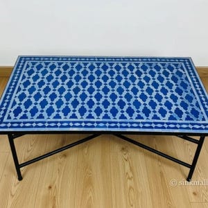 May include: Rectangular coffee table with a blue and white geometric tile top. The table has a black metal frame and legs. The tile design features a repeating pattern of diamond shapes. A stylish accent piece for any living room.