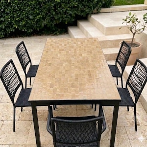 Puede incluir: Una mesa de comedor rectangular con una superficie de azulejos en tonos beige claro y un marco de metal negro, acompañada de cuatro sillas negras con respaldo de celosía tejida y patas de metal negro para uso en exteriores.