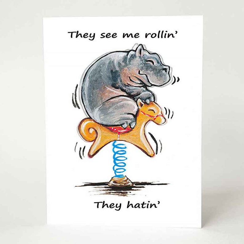 a greeting card with a smiling hippo, riding an orange rocking horse. the card reads, "they see me rollin'. they hatin'"