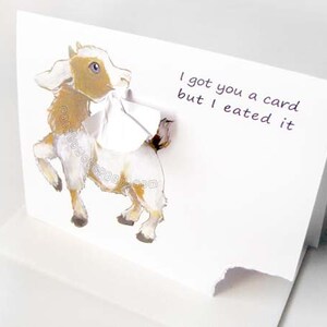 May include: A white greeting card with a 3D illustration of a goat. The goat is brown, white, and tan with blue eyes. The card reads, "I got you a card but I eated it."