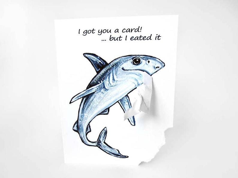 May include: A humorous greeting card featuring a cartoon shark with a torn edge, the text reads "I got you a card! ... but I ate it."