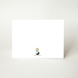 May include: A blank white card with a black silhouette of a cat holding a rainbow balloon. The text "rainbowcatmag.com" is printed in black at the bottom of the card.