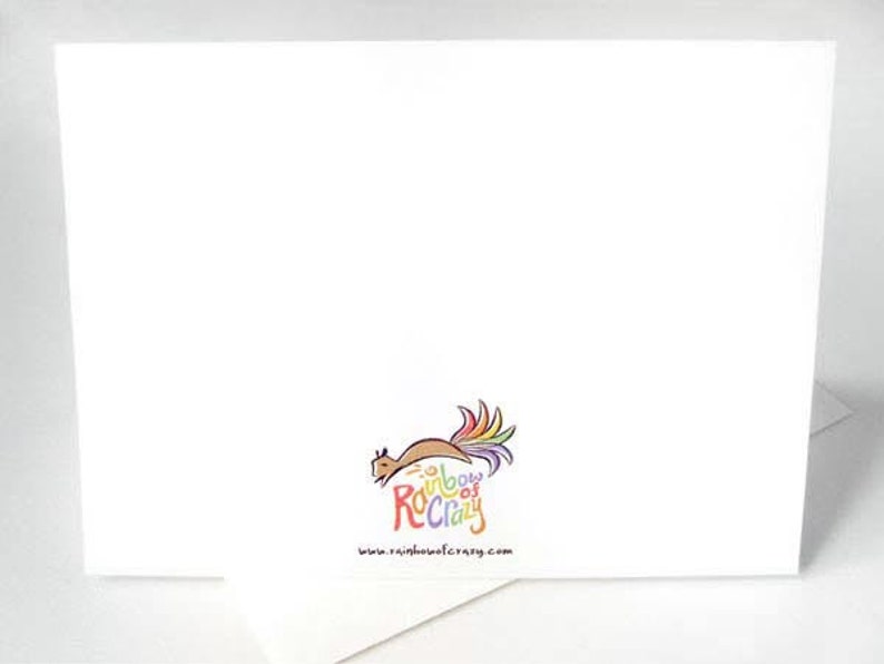 May include: A white greeting card with the "Rainbow of Crazy" logo, featuring a squirrel with a rainbow tail. The website address www.rainbowofcrazy.com is printed below the logo. The card is on a white surface.