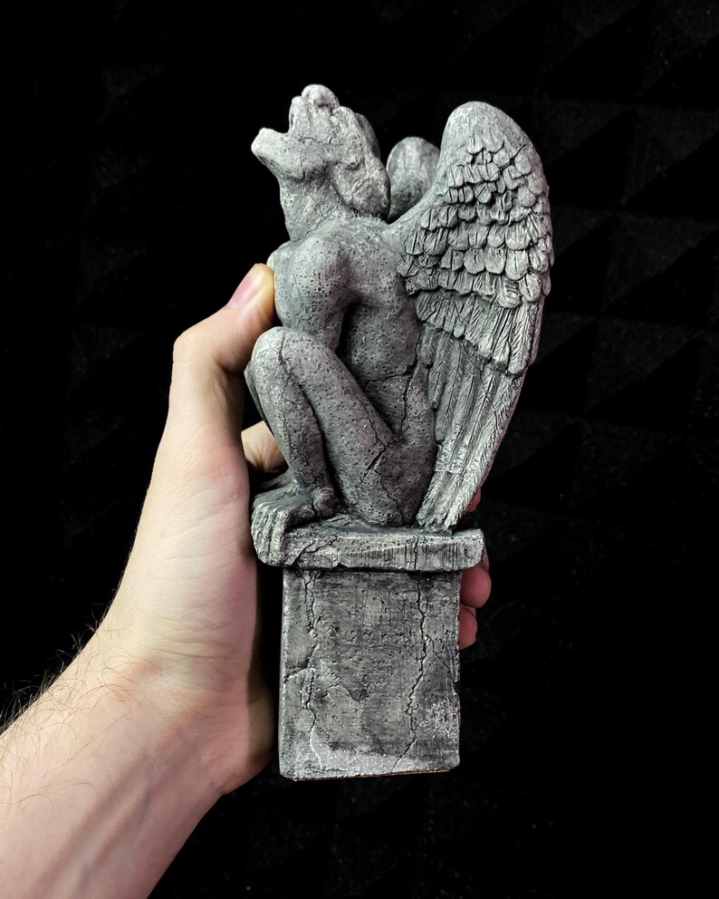 K&ouml;nnte beinhalten: Graue Gargoyle-Statue mit detaillierten Fl&uuml;geln, auf einem Steinsockel. Die Statue hat ein verwittertes Aussehen mit sichtbaren Rissen und einer strukturierten Oberfl&auml;che. Die Gargoyle befindet sich in einer hockenden Position mit offenem Mund.