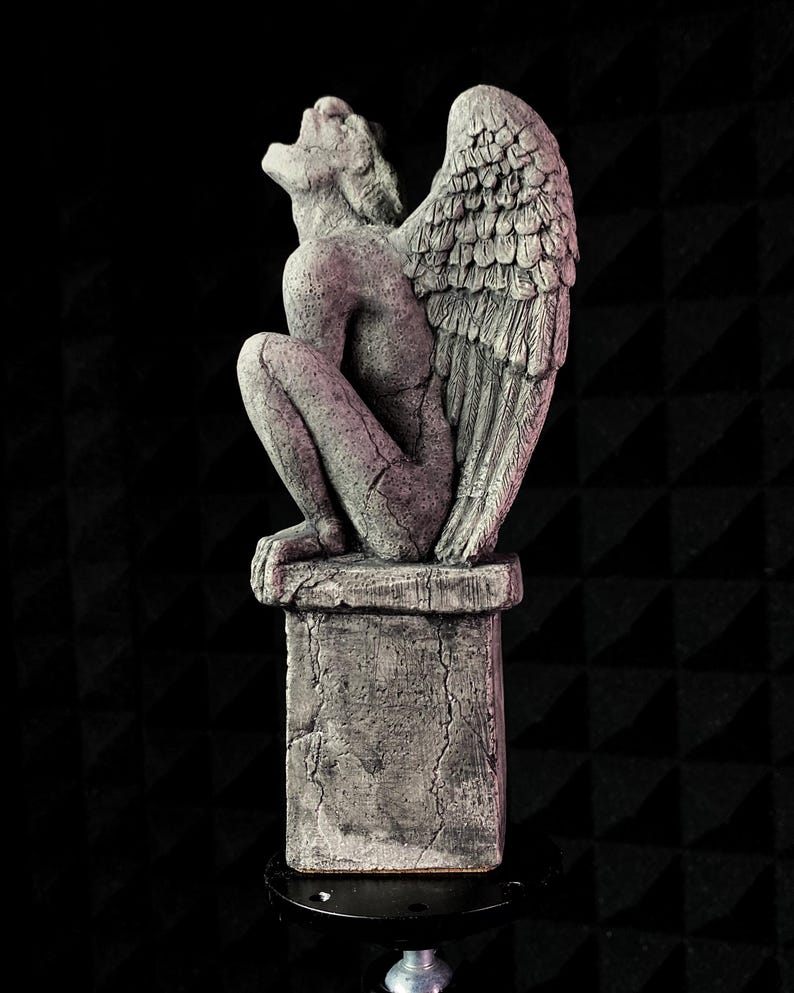 K&ouml;nnte beinhalten: Graue Stein-Wasserspeier-Statue mit gro&szlig;en Federfl&uuml;geln, die auf einem verwitterten Sockel sitzt. Die Statue befindet sich in einer hockenden Position, mit zur&uuml;ckgeneigtem Kopf und offenem Mund. Der Hintergrund ist schwarz.