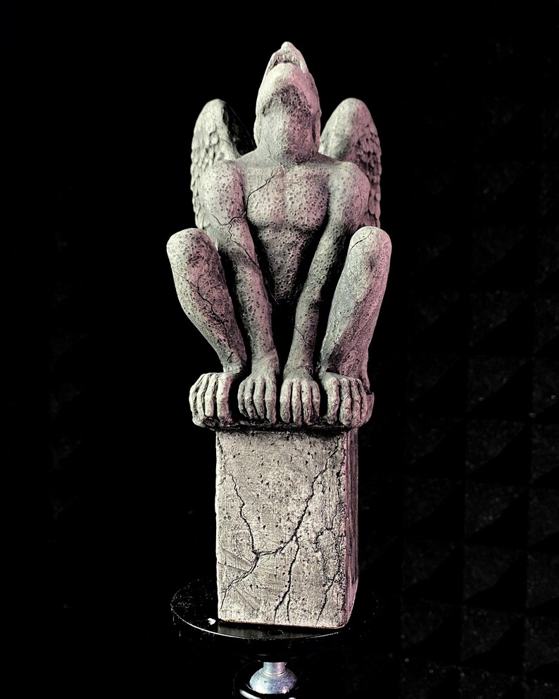 K&ouml;nnte beinhalten: Eine graue Gargoyle-Statue mit ausgebreiteten Fl&uuml;geln, die auf einem verwitterten Steinsockel sitzt. Die Statue hat einen muskul&ouml;sen Torso und blickt nach oben. Die Statue ist etwa 25 cm hoch.