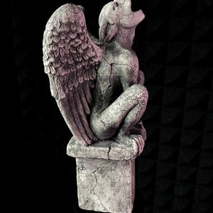K&ouml;nnte beinhalten: Graue Gargoyle-Statue mit gro&szlig;en, detaillierten Fl&uuml;geln und einem rissigen, verwitterten Aussehen. Die Statue sitzt auf einem quadratischen Sockel, mit zur&uuml;ckgeneigtem Kopf und offenem Mund. Die Skulptur ist aus Stein.
