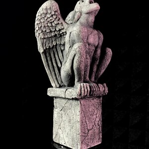 K&ouml;nnte beinhalten: Graue Gargoyle-Statue mit gro&szlig;en, detaillierten Fl&uuml;geln und rissigem, verwittertem Aussehen. Die Statue thront auf einem quadratischen Sockel mit &auml;hnlicher Textur, vor schwarzem Hintergrund. Die Gargoyle blickt nach oben.