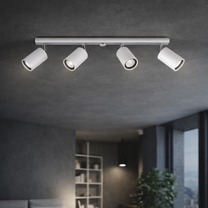 May include: A white track lighting fixture with four adjustable spotlights. The fixture is mounted on a grey ceiling. The spotlights are angled downwards. The room has a minimalist design with large windows.