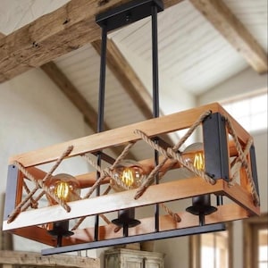 Può includere: Un lampadario rettangolare in legno con tre lampadine a vista. L'apparecchio ha una struttura in legno naturale, dettagli in metallo nero e dettagli in corda. Le lampadine sono rotonde ed emettono una luce calda e gialla. L'apparecchio è sospeso al soffitto.