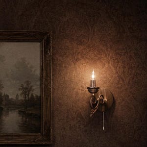 Puede incluir: Un aplique de pared con acabado metálico oscuro y una bombilla única en forma de vela. El accesorio presenta un brazo curvo, una placa circular y una cadena de tiro blanca. Está montado sobre una pared marrón con un patrón de damasco.
