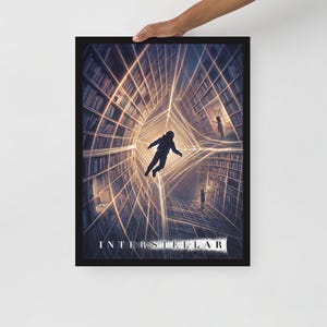 May include: Framed art print featuring a surreal, sci-fi scene with an astronaut floating in a library-like structure. The artwork has a dark color palette with glowing lines and the word "INTERSTELLAR" at the bottom.