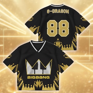 Puede incluir: Camiseta de malla negra con detalles dorados y ribete blanco. La camiseta presenta el texto "G-DRAGON" y el número "88" en la espalda. La parte delantera muestra un logotipo de corona con el texto "BIGBANG".