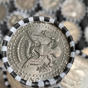 May include: A silver-colored United States half dollar coin featuring an eagle design on the reverse side, encased in a paper coin roll wrapper with alternating black and white stripes. The coin shows the text UNITED STATES OF AMERICA HALF DOLLAR.
