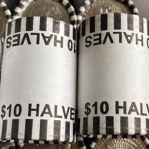 May include: Close-up of two rolls of $10 half dollars. The white paper rolls have black vertical stripes at the top and bottom. The text "$10 HALVES" is printed in black on the rolls. The image shows the edges of the coins.