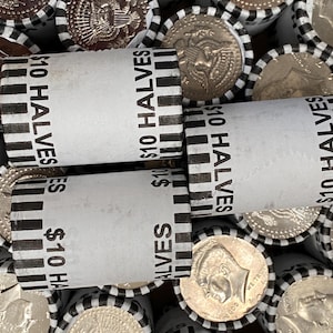 May include: Multiple cylindrical paper coin rolls filled with United States half-dollar coins. Each white wrapper features black vertical stripes and the printed text $10 HALVES. The ends of the rolls reveal the metallic silver surfaces of the coins.
