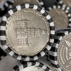 May include: A silver-colored United States half dollar coin featuring Independence Hall, encased in a white paper coin roll wrapper with black stripes. The coin shows the text 200 YEARS OF FREEDOM, INDEPENDENCE HALL, and E PLURIBUS UNUM.