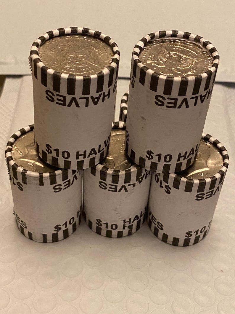 May include: Five cylindrical paper rolls of United States half-dollar coins stacked in a pyramid formation. Each white wrapper features black vertical stripes at the top and bottom edges, with the printed text $10 HALVES visible on each roll.