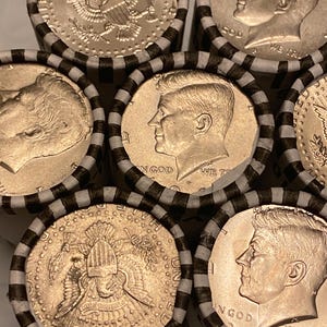 May include: Several rolls of United States half-dollar coins wrapped in white paper with black stripes. The visible coins feature the profile of John F. Kennedy and the presidential seal, with the text IN GOD WE TRUST clearly visible on the faces.