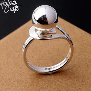 Puede incluir: Una taza de cerámica blanca con un asa negra y el texto "But First, Coffee" en un estilo manuscrito. La taza está sobre una superficie blanca. La taza mide aproximadamente 10 cm de alto.