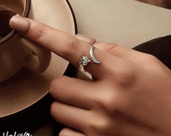May include: A silver ring featuring a fox head and a crescent moon design. The ring is worn on a finger, showcasing the detailed craftsmanship of the jewelry. The ring is a unique piece of jewelry.