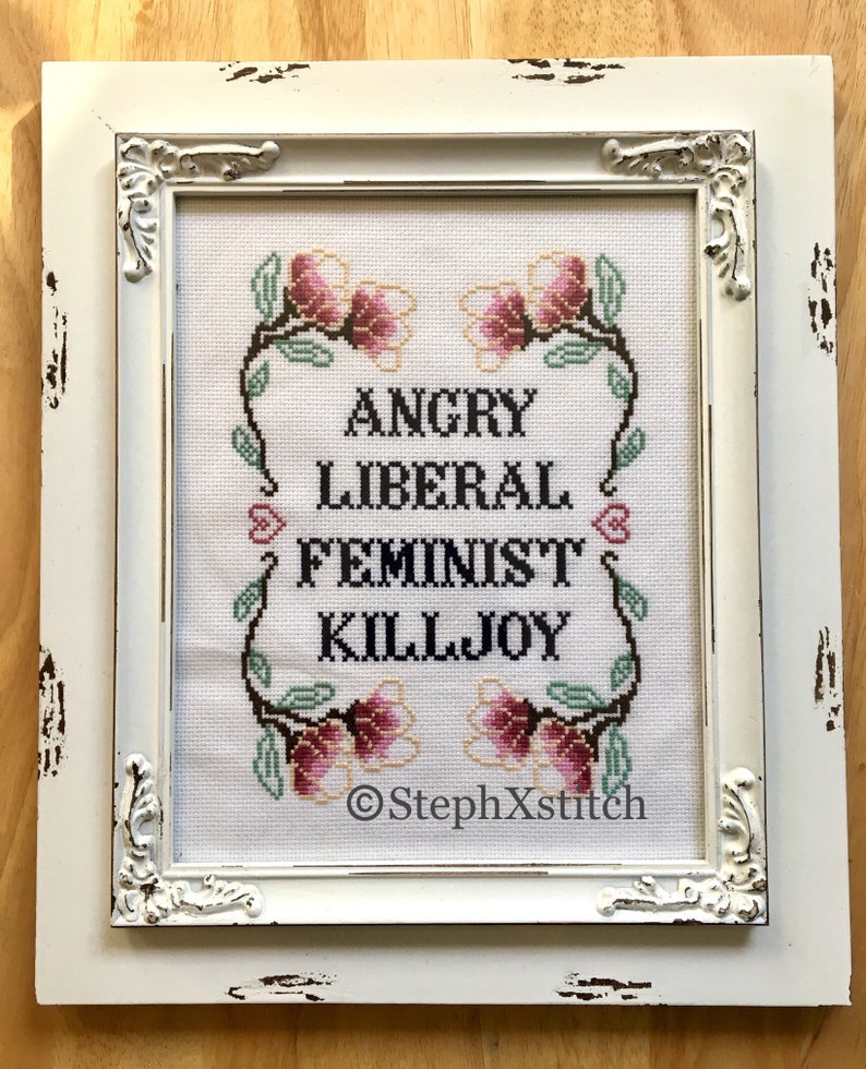 May include: White framed cross-stitch with pink flowers and the text "Angry Liberal Feminist Killjoy" and the signature "StephXstitch".