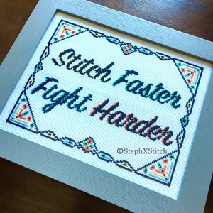 May include: Cross-stitch art in a gray frame. The white fabric features the text "Stitch Faster Fight Harder" in blue, green, and orange. A decorative border with floral accents surrounds the text. The artist's name, StephXStitch, is in the bottom right corner.