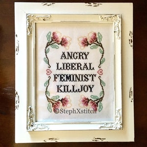 May include: White framed cross-stitch embroidery with pink flowers and the text "Angry Liberal Feminist Killjoy" and the signature "StephXStitch".