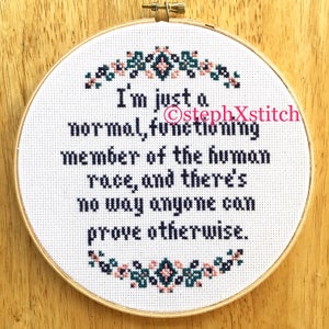 May include: A cross-stitch embroidery in a wooden hoop. The white fabric features the text "I'm just a normal, functioning member of the human race, and there's no way anyone can prove otherwise." Floral accents are at the top and bottom.
