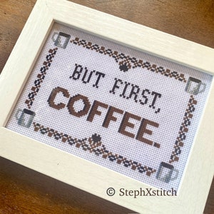 Könnte beinhalten: Weiß gerahmte Kreuzstich-Stickerei mit braunem und schwarzem Garn. Die Stickerei lautet "But first, coffee." mit einem Kaffeetassen-Design in der Ecke. Die untere rechte Ecke trägt das Copyright-Symbol und den Text "StephXStitch".