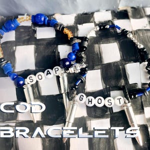 May include: Two beaded bracelets with the text "SOAP" and "GHOST" spelled out in white letter beads. The bracelets feature blue, black, and silver beads, and silver bullet-shaped charms. The words "COD BRACELETS" are in the image.