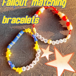 May include: Two beaded bracelets with the text "Fallout matching bracelets". One bracelet is blue and yellow with star-shaped beads. The other is red, white, and yellow with the text "NUKA COLA".