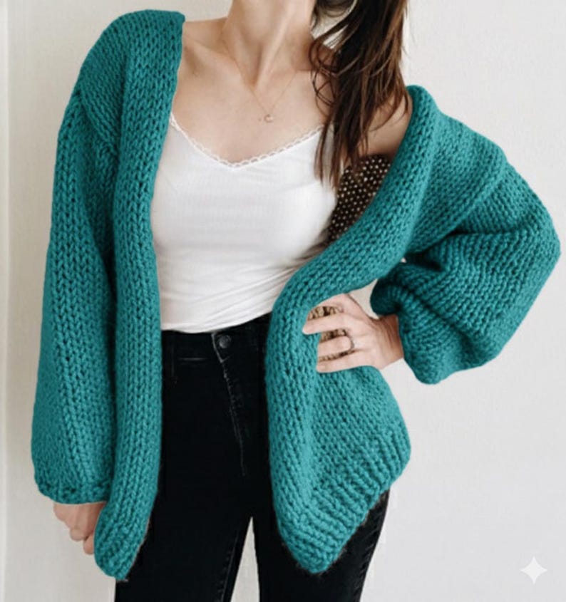 Puede incluir: Un c&aacute;rdigan de punto grueso de color verde azulado con mangas largas. El su&eacute;ter abierto est&aacute; hecho de un hilo grueso y tiene un ajuste relajado. La modelo lleva una camiseta sin mangas blanca y vaqueros negros.