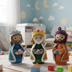 Puede incluir: Tres figuras de los Reyes Magos hechas a ganchillo. Las figuras visten túnicas azules, verdes y naranjas, cada una con una corona y sosteniendo un pequeño regalo. Las figuras tienen barbas marrones y están ambientadas en un cuarto infantil.