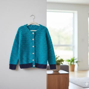 Puede incluir: Un c&aacute;rdigan tejido a mano de color azul turquesa, con cuello redondo y mangas largas, colgado de una percha blanca. El c&aacute;rdigan presenta un patr&oacute;n de puntadas texturizadas, una fila de botones rosas y ribetes azul marino en los pu&ntilde;os y el dobladillo. Este su&eacute;ter es perfecto para combinar.