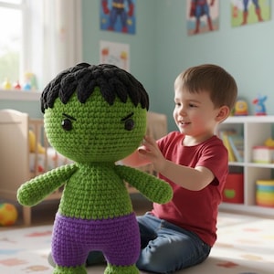 Könnte beinhalten: Handgemachte, grüne und lila gehäkelte Hulk-Puppe mit schwarzen Haaren. Die Puppe hat einen großen Kopf, kleine Arme und Beine. Die Puppe befindet sich in einem Kinderzimmer mit Superhelden-Postern an der Wand.