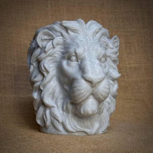 May include: A detailed, white marble lion head sculpture. The lion's mane is intricately carved, and the sculpture has a weathered appearance. The sculpture is set against a neutral background, highlighting the details of the lion's face.